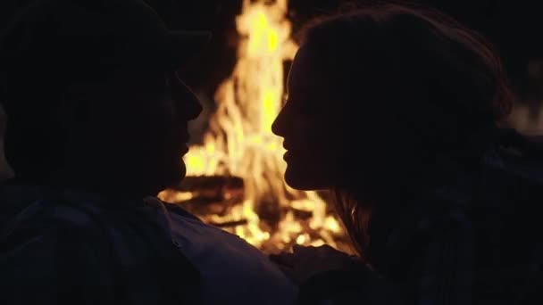 若いカップルのシルエットは、たき火とキスの近くに横たわって、屋外で — ストック動画