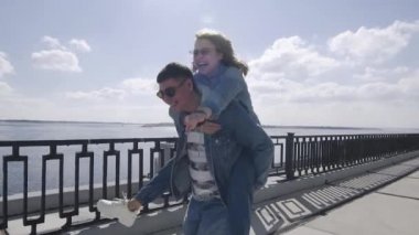 Genç adam sırtında bir kadın taşıyor ve gezinti güvertesinde koşuyor.