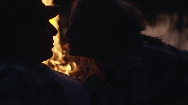 Silhouettes de jeune couple repose près du feu de joie regarde dans les yeux de l'autre et baiser, à l'extérieur — Video