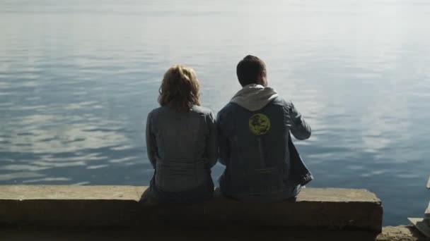 Back view of beautiful romantic couple of man and woman sits near river and feeds seagulls — Stock Video