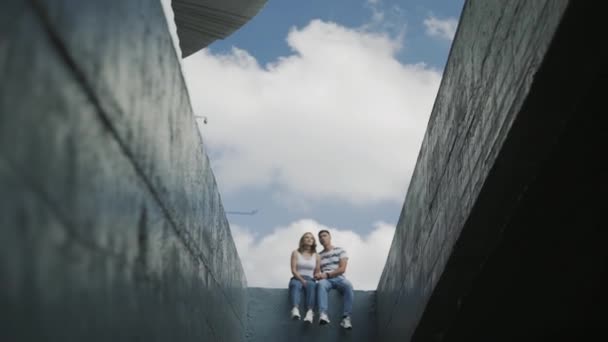 Unga attraktiva par i blå jeans sitter på betongvägg — Stockvideo
