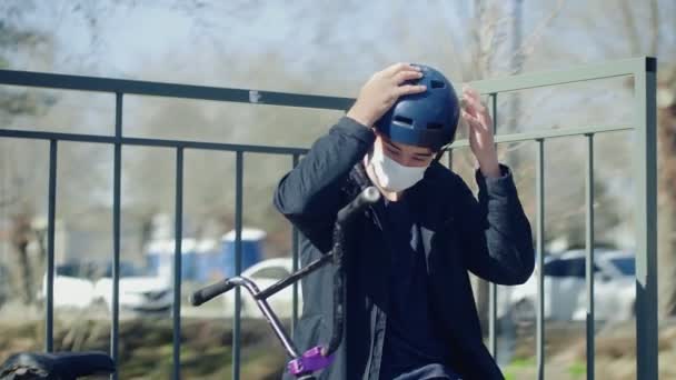 Ένας νεαρός αναβάτης BMX με ιατρική μάσκα κάθεται σε μια ράμπα και φοράει κράνος — Αρχείο Βίντεο