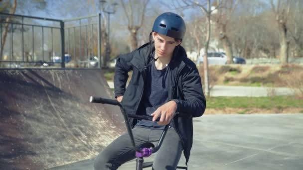 En ung bmx ryttare sitter på en cykel och talar på spartphone — Stockvideo