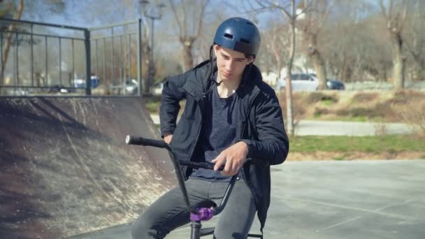 Un joven jinete de bmx sentado en una bicicleta y hablando por el spartphone — Vídeos de Stock