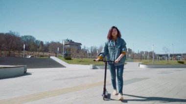 Genç Asyalı kadın yaz parkında scooterla yürüyor.