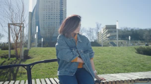 Joven asiática mujer se sienta en el banco y habla el teléfono inteligente en el parque de verano — Vídeo de stock