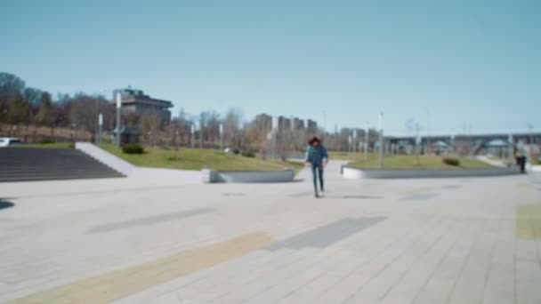 Giovane donna asiatica in una giacca jeans cavalca uno scooter nel parco estivo — Video Stock