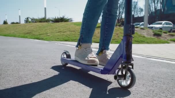 Close up of womans legs in jeans pants rides on the scooter in a summer park — Stock Video