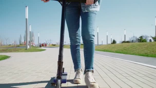 Primer plano de las piernas de las mujeres en pantalones vaqueros camina con la moto en un parque de verano — Vídeo de stock