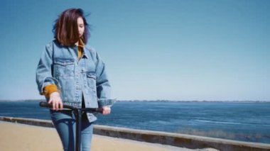 Kot ceketli genç Asyalı kadın mobiletiyle yürüyüp yaz parkında selfie çekiyor.