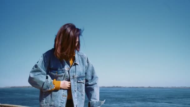 Jonge aziatische vrouw in een jeans jas loopt met de scooter en neemt selfies in een zomer park in de buurt van de rivier — Stockvideo