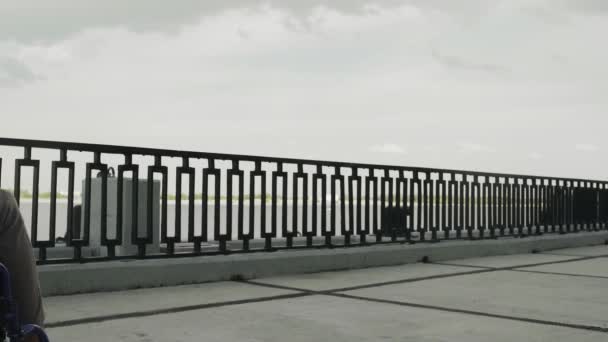 Young man disabled in wheelchair rides along the promenade — Stock Video