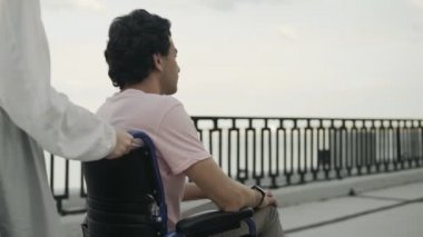 Engelli bir adama yardım eden bir kadın. Tanınmayan bir kadın engellilerle ilgileniyor ve tekerlekli sandalyesiyle parkta dinlenmesine yardım ediyor..