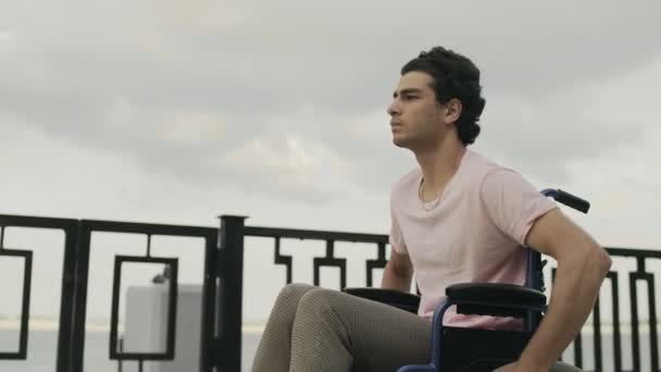 Der unglückliche Mann sitzt im Rollstuhl. Traurige Rollstuhlfahrt auf der Promenade — Stockvideo