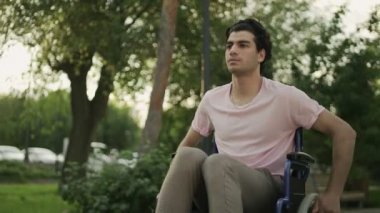 Tekerlekli sandalyedeki engelli genç adam parkta geziyor..
