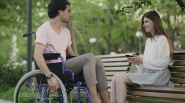 Tekerlekli sandalyedeki genç adam ve parkta buluşan kadın.