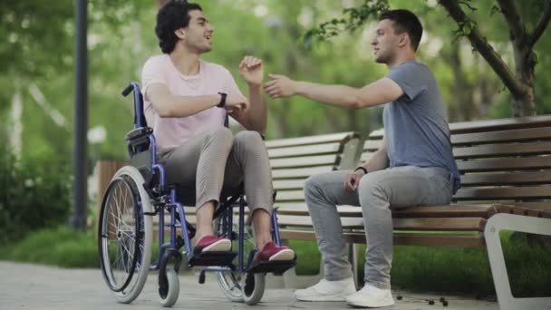 Egy tolószékes fiatalember találkozik a barátjával a parkban.. — Stock videók