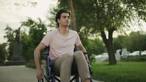 Behinderter junger Mann im Rollstuhl fährt in Park. — Stockfoto