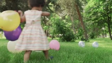 Küçük Afro-Amerikalı kız parkta renkli balonlarla oynuyor..