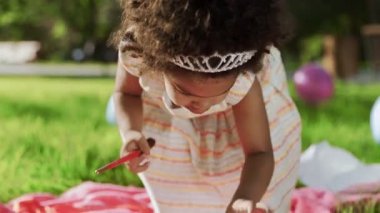 Küçük Afrikalı kız, arka planda renkli balonlarla parkta fırça ve kalemlerle oynuyor.