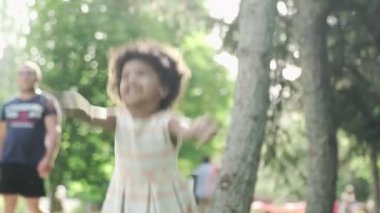Küçük Afro-Amerikalı kız parkta oynar ve zıplar. Arka planda tanınmayan insanlar