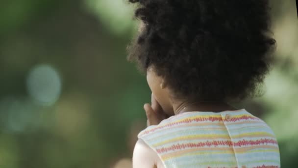 En liten afrikansk-amerikansk flicka med diadem på huvudet som äter och viftar med händerna som en fågel — Stockvideo