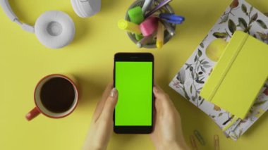 Eller yukarı. Masasında yeşil ekranı olan akıllı telefonunu kullanan bir kadın. Haberler, fotoğraflar. Ofis masası geçmişi.