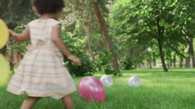 Küçük Afro-Amerikalı kız parkta renkli balonlarla oynuyor..
