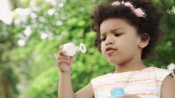 Petite et mignonne fille afro-américaine souffler des bulles de savon dans le parc . — Video