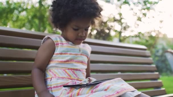 Chica afroamericana descontenta está viendo dibujos animados en la tableta en el parque — Vídeos de Stock