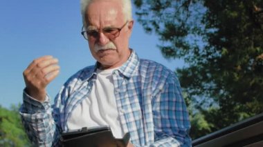 Bıyıklı yaşlı bir adam kitap okuyor. Yaşlı bir adam sıcaktır ve elleriyle yüzünü siler.