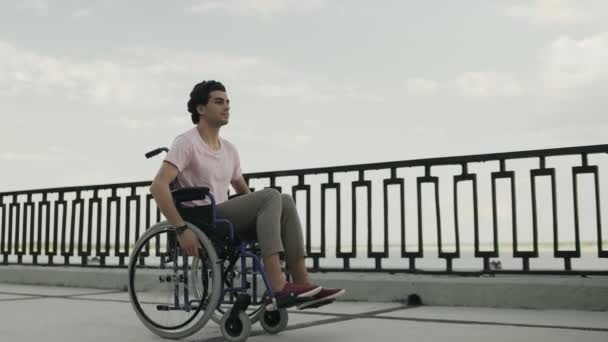 Der unglückliche Mann fährt mit dem Rollstuhl die Promenade entlang — Stockvideo