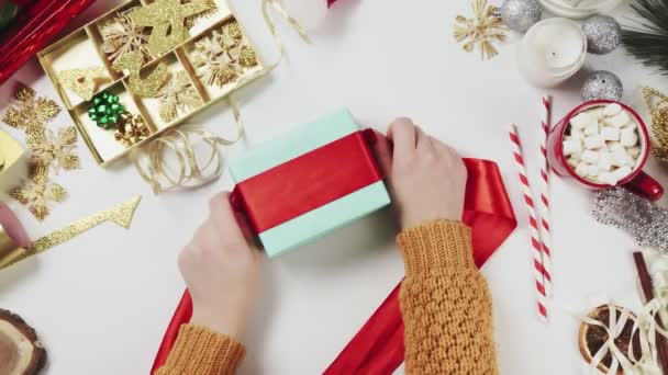 Γυναίκα περιτύλιγμα χριστουγεννιάτικο δώρο, δώρο σε λευκό φόντο τραπέζι με διακοσμήσεις διακοπών. — Αρχείο Βίντεο