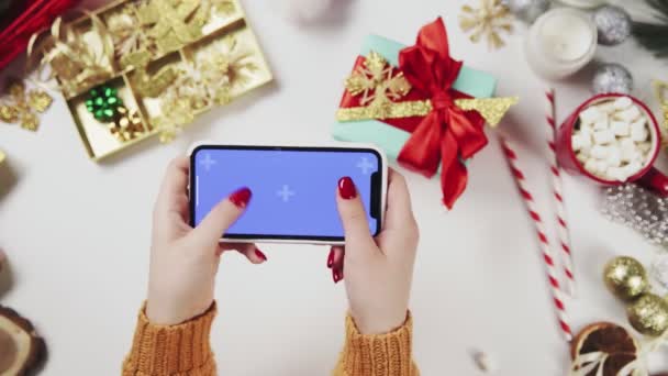 Mujer usando el teléfono inteligente con la tecla Chroma, tocando, deslizar, desplazarse hacia arriba. Decoración navideña sobre fondo de mesa blanco . — Vídeos de Stock