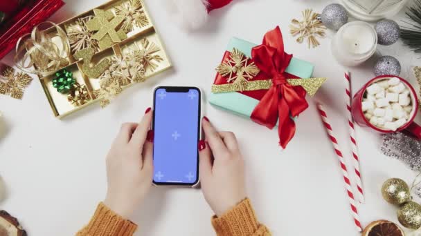 クロマキーでスマートフォンを使用して女性,タップ,スワイプ,上にスクロール.白いテーブルの背景にクリスマスの休日の装飾. — ストック動画