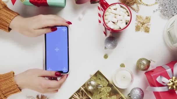 Woman using smartphone with Chroma key, tapping, swipe, scrolling up. Christmas holiday decoration on white table background. Vertical Screen Orientation Video 9:16