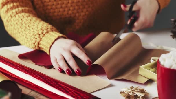 Frau schneidet rotes Papier zum Einwickeln von Weihnachtsgeschenken auf Tisch mit Weihnachtsdekoration. — Stockvideo