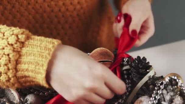 Mujer irreconocible decorando corona navideña con cinta roja — Vídeo de stock