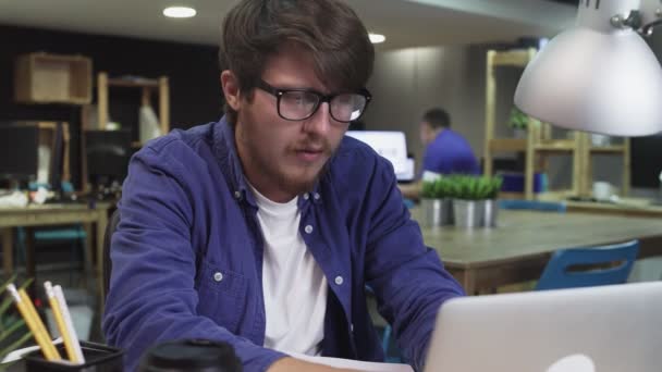 Ενοχλημένος προγραμματιστής με γυαλιά που εργάζεται στο lap-top στο γραφείο — Αρχείο Βίντεο