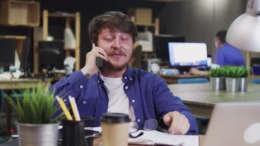 Ofiste otururken telefonda konuşan mutlu genç adam..