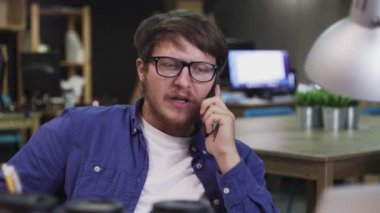 Genç adam cep telefonuyla konuşuyor ve yaratıcı ofisteki not defterine not alıyor..
