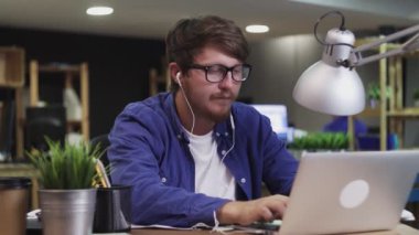 Kulaklıklı genç programcı müzik dinliyor ve ofiste dizüstü bilgisayarla çalışıyor.