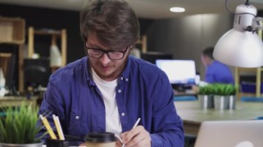 Modern ofiste çalışan genç bir iş adamı. Not al, bilgisayara yaz ve ara.
