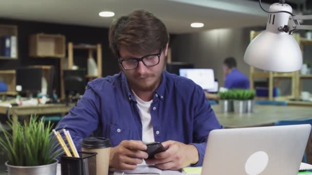 Επιχειρηματίας κάθεται στο γραφείο του Εργάζεται σε επιτραπέζιο υπολογιστή στο κομψό γραφείο, μαζεύει και ξεκινά Χρησιμοποιώντας Smartphone, Χρησιμοποιεί την εφαρμογή Social Media, Emailing Business Partners, Μηνύματα. — Αρχείο Βίντεο