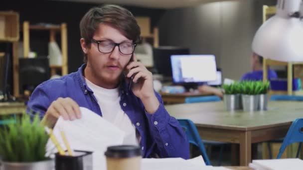 Jonge zakenman praat over mobiele telefoon en controleert jaarrekening op kantoor — Stockvideo