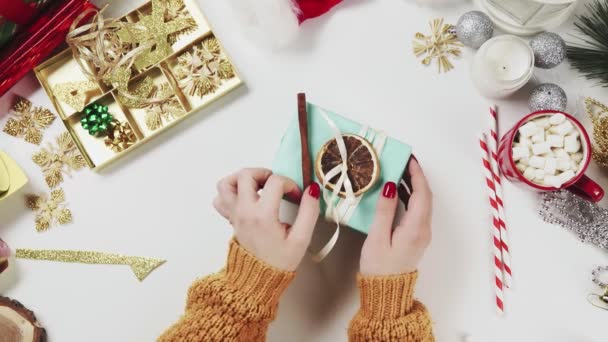 Frau wickelt Weihnachtsgeschenk ein und dekoriert es mit trockenem Orange und kleiner Weihnachtskugel — Stockvideo