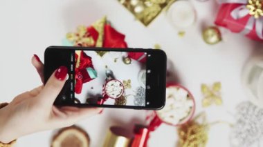 Akıllı telefondan güzel fotoğraf çeken bir kadın. Beyaz masada bayanların Noel hediyelerini fotoğraflayan elleri. Dikey Ekran Yönlendirme Videosu 9: 16