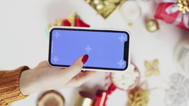 Woman using smartphone with Chroma key, tapping, swipe, scrolling up. Christmas holiday decoration on white table background. Vertical Screen Orientation Video 9:16 — Stock Video