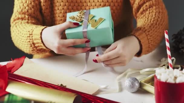 Жіночі руки обгортають різдвяний подарунок у синьому папері та зав'язують стрічкою — стокове відео