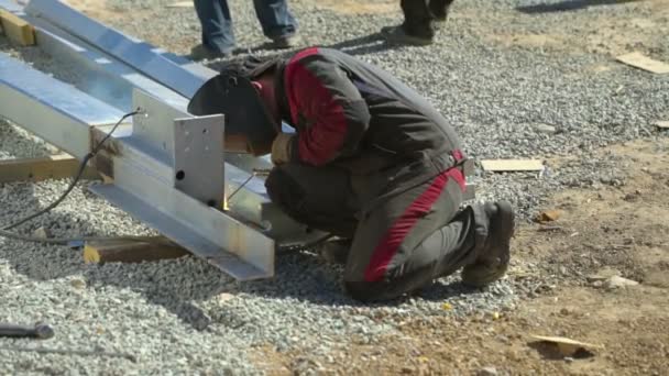 Soldador de hombre suelda las partes de la estructura en el sitio de construcción — Vídeos de Stock